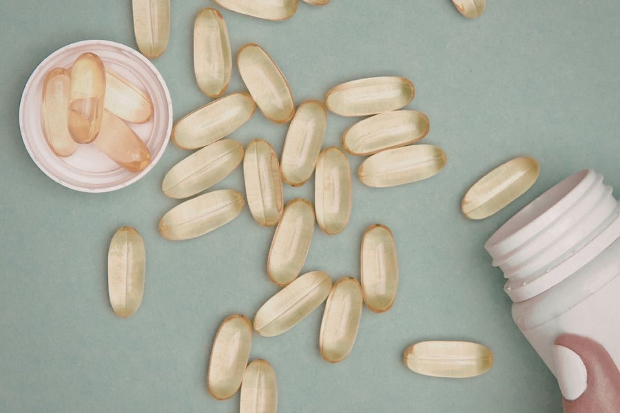 Golden softgel capsules scattered across a sea green surface beside a white supplement bottle and lid